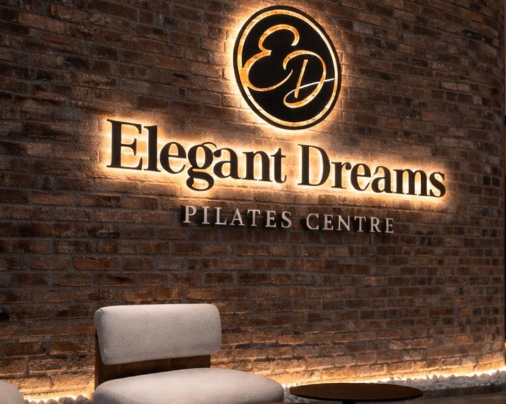 A backlit "ED" roundel and Elegant Dreams Pilates Centre lettering glowing on a reclaimed-brick wall.