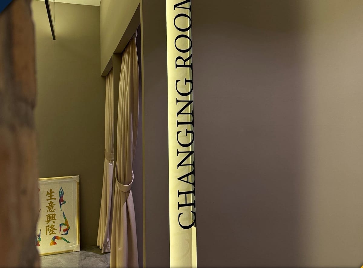 A slim vertical backlit panel reading CHANGING ROOM mounted flush on a warm plaster wall beside a curtained doorway.
